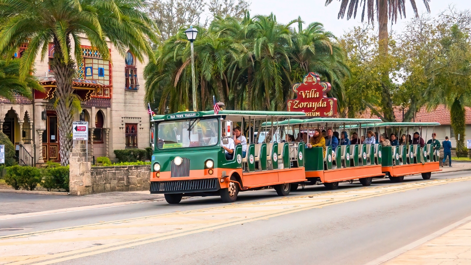Adult visitors riding a trolley past Villa Zorayda Museum, the former winter home of a Boston millionaire, during a tour of downtown highlights in this historic city. The trolley tour showcases notable landmarks and attractions in St. Augustine, Florida, catering to tourists and history enthusiasts.