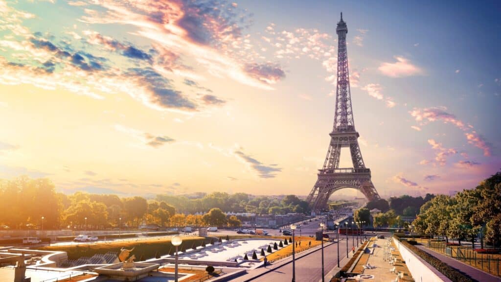 A photograph capturing the view of the gardens Trocadero and the Eiffel Tower during sunrise in Paris. The image features the iconic Eiffel Tower in the background, illuminated by the early morning light. The gardens Trocadero are visible in the foreground, showcasing the landscaping and pathways typical of the area.