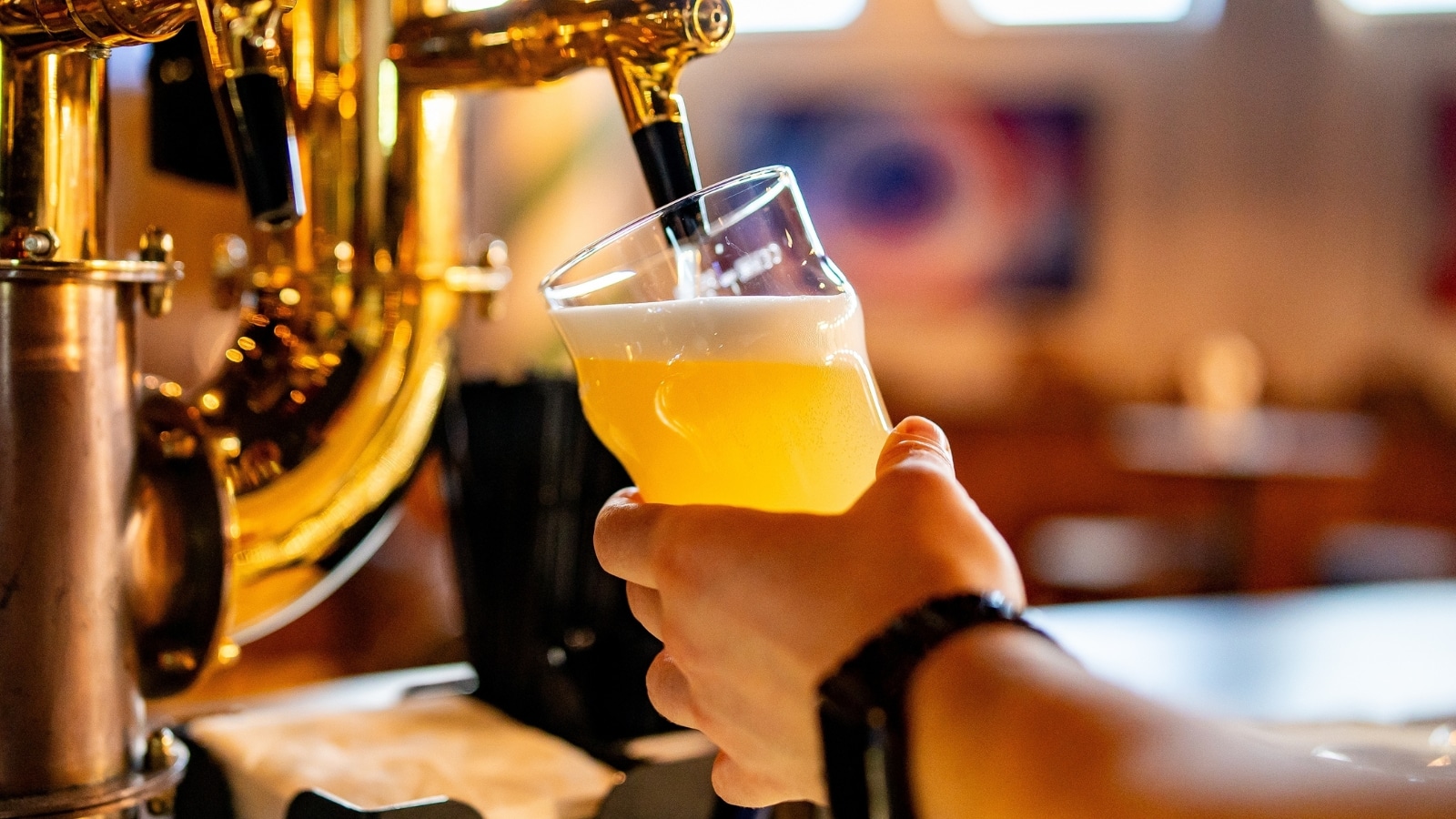 A photograph capturing a man bartender's hand operating a beer tap to pour beer into a glass in a bar or pub setting.