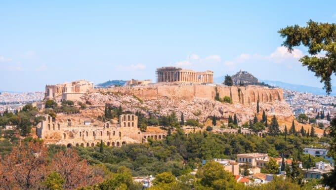 A photograph showcasing The Acropolis of Athens and the Parthenon. The image features the iconic ancient structures against a clear sky, highlighting the enduring architectural significance of these historical landmarks.
