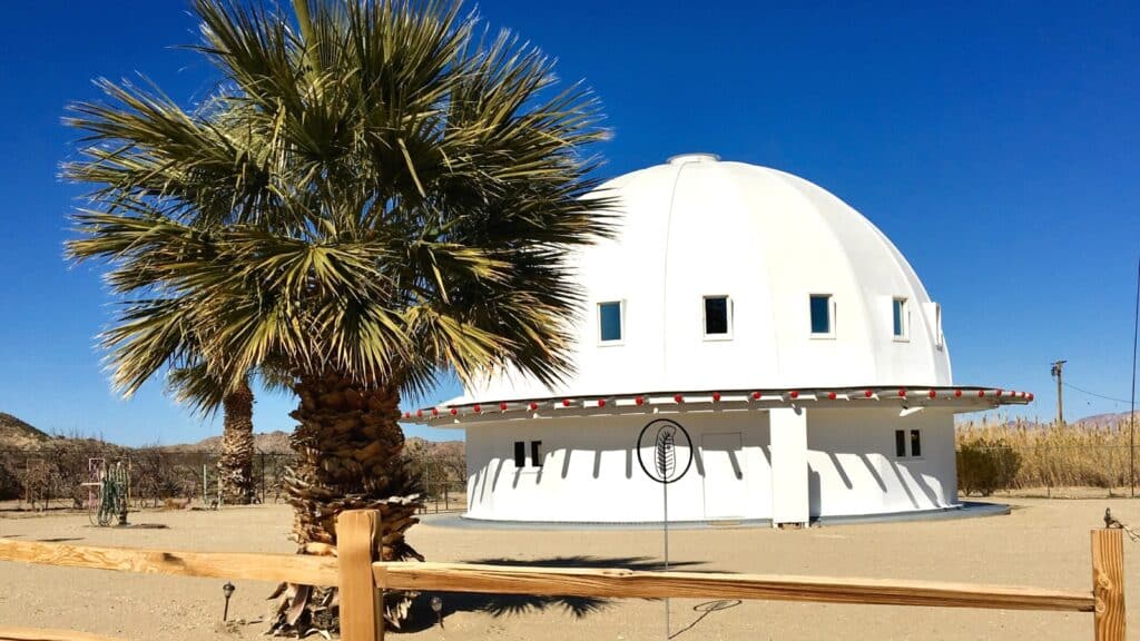A photograph depicting the iconic Integratron structure in Landers, California, under an intense blue desert sky. The image showcases the architectural profile of the Integratron, a notable landmark known for its unique design and historical significance.