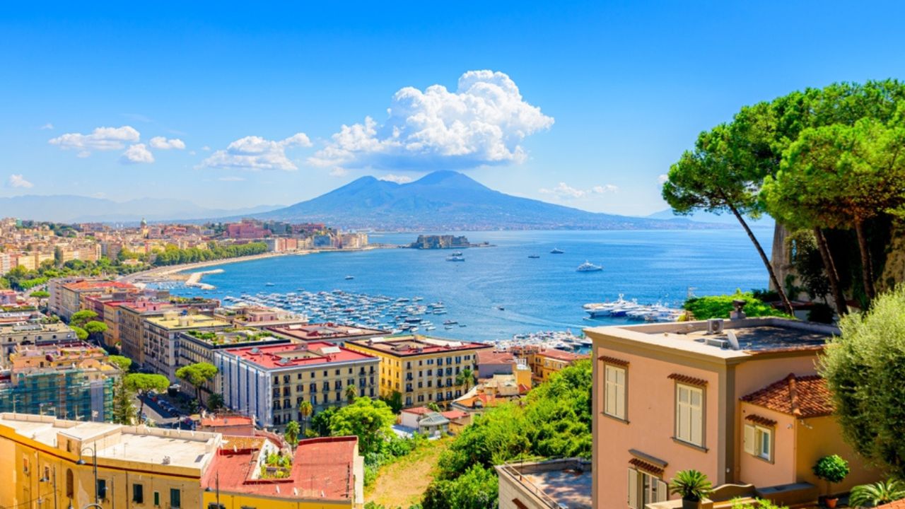 Naples, Italy. View of the Gulf of Naples from the Posillipo hill with Mount Vesuvius far in the background and some pine trees in foreground. August 31, 2021.