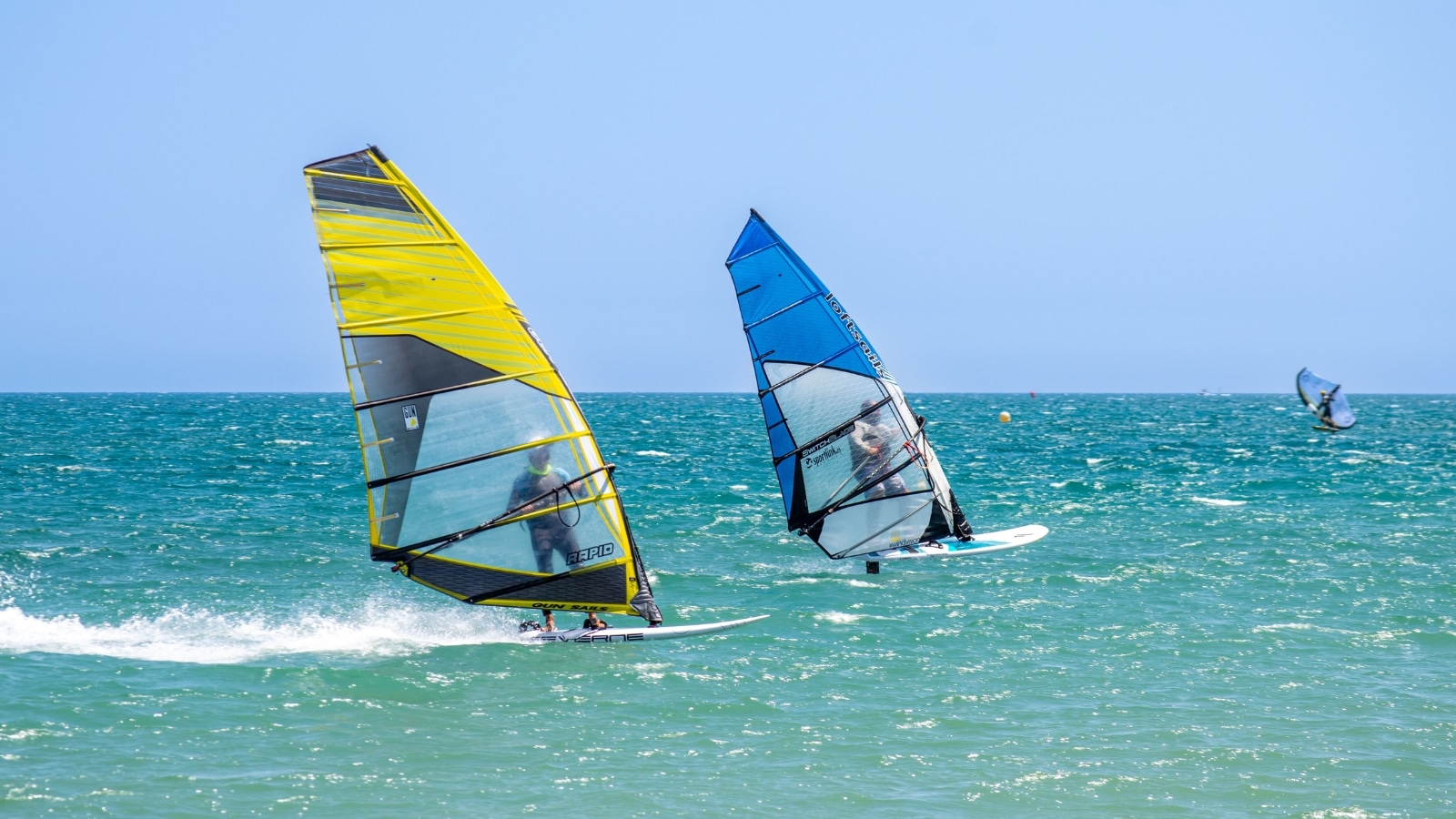 A photograph depicting two kiteboarders on the water, each on boards of distinct colors—one yellow, the other blue. The image captures a moment of recreational kiteboarding, showcasing the participants engaged in the sport.