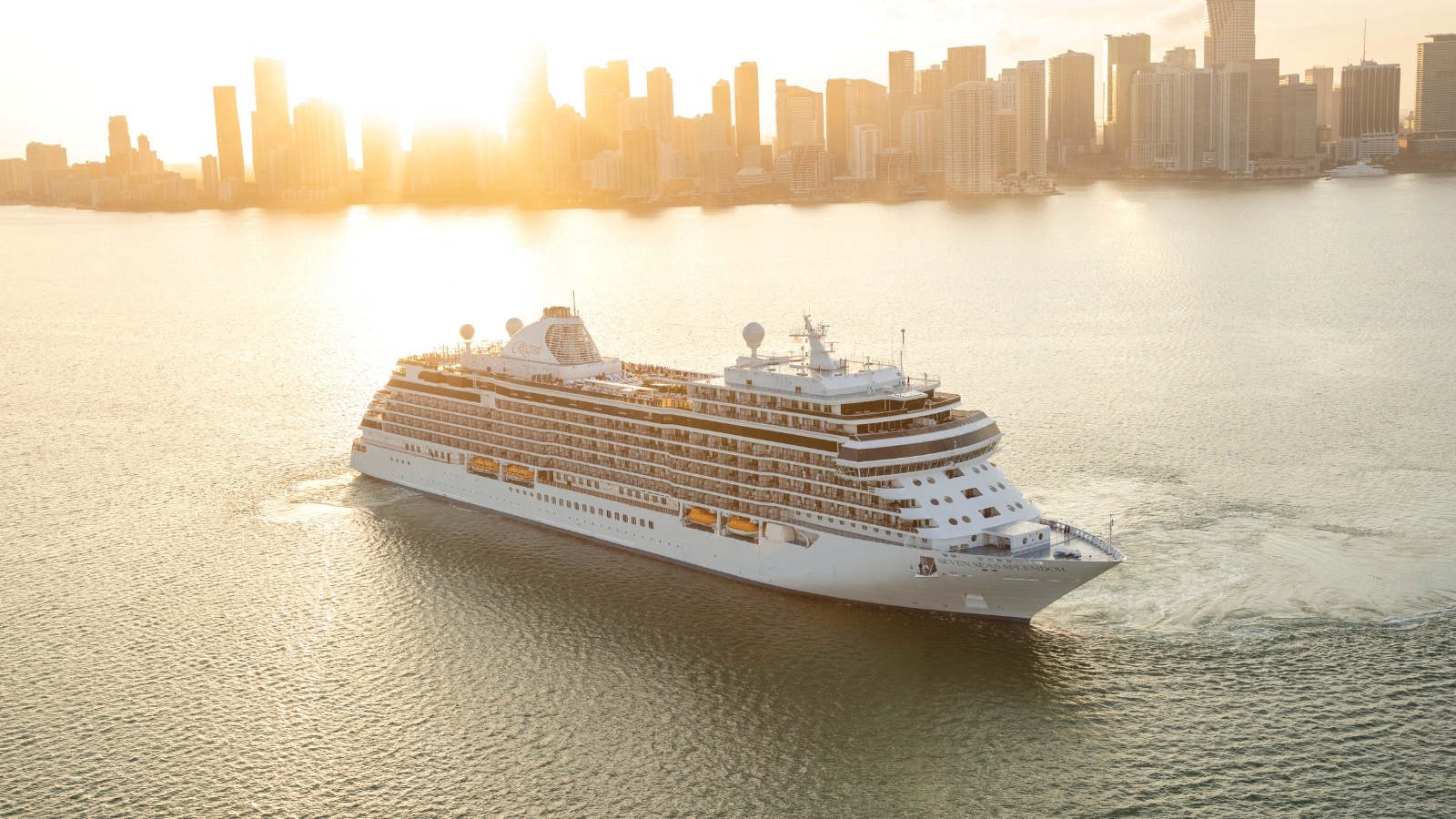 The image captures a large cruise ship against the backdrop of a city skyline dominated by high-rise buildings. The scene is enhanced by a bright sunrise in the background. The focus is on the juxtaposition of the massive ship against the urban landscape and the natural light of dawn.