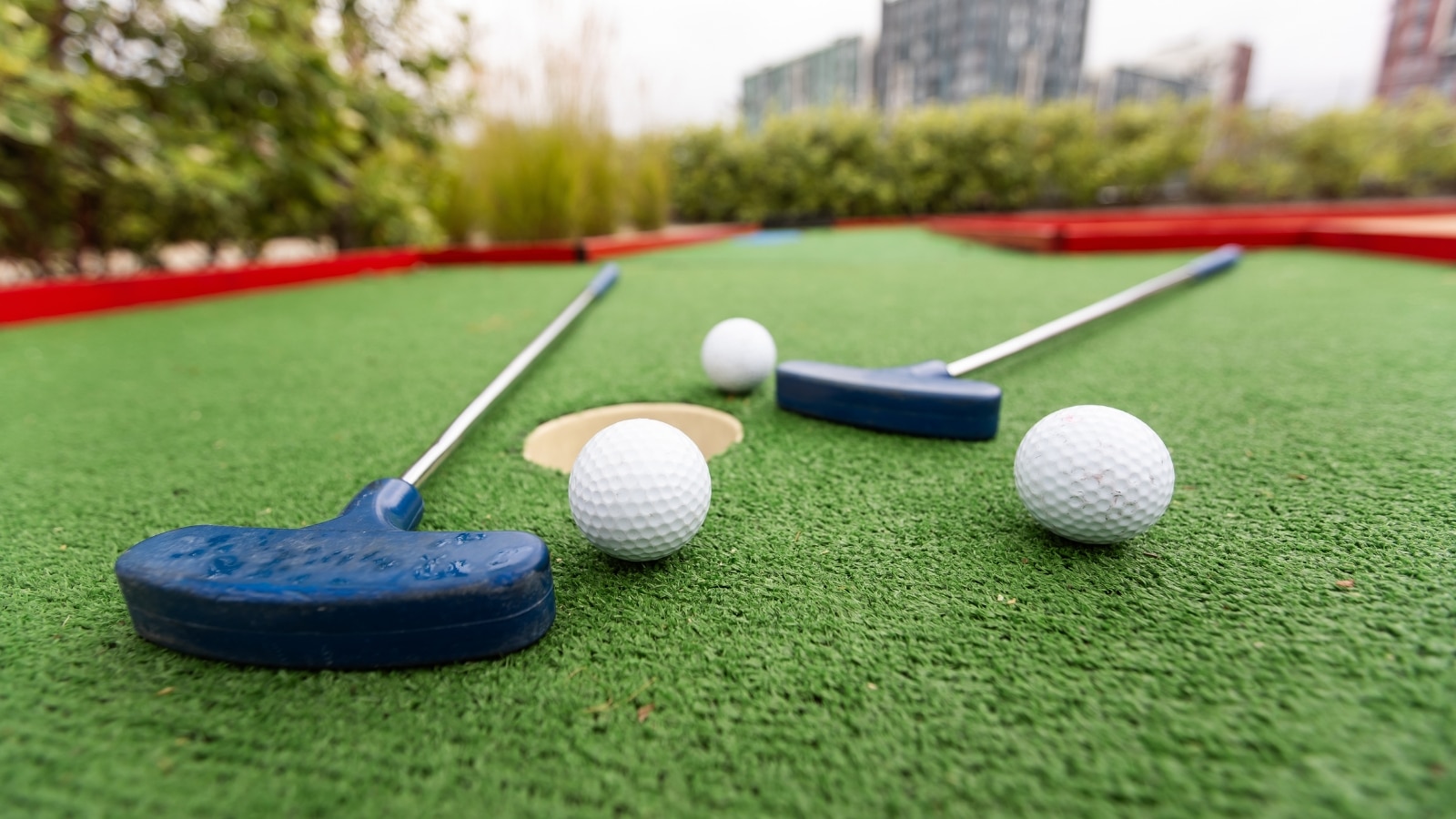 A close-up photograph capturing two golf clubs and two golf balls resting on the grass at a mini golf course.