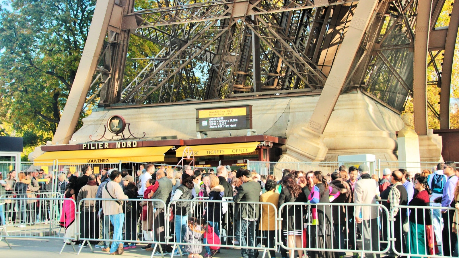 A photograph showing a queue of tourists waiting to purchase tickets to access the Eiffel Tower landmark.