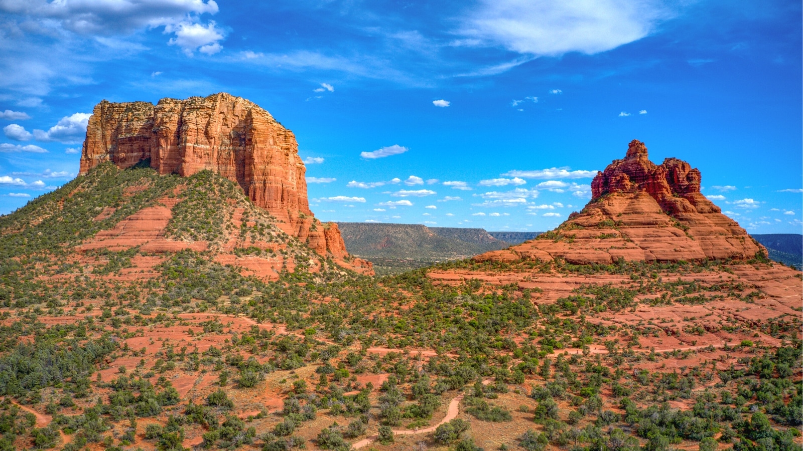 A photograph depicting rock formations in an arid area of Sedona, Arizona, under a clear blue sky. The image showcases the rugged geological features typical of the region, including red rock formations and cliffs.