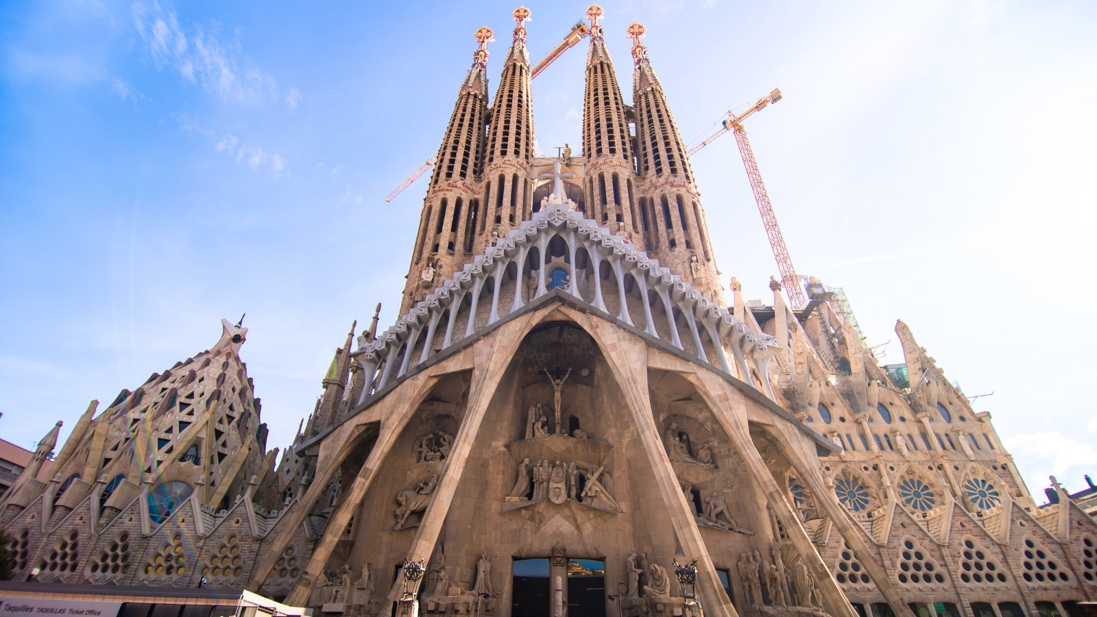 A front view photograph capturing the Sagrada Familia basilica in Barcelona, Spain. The image showcases the iconic architectural features of the basilica, including its towering spires, intricate facades, and distinctive sculptures.