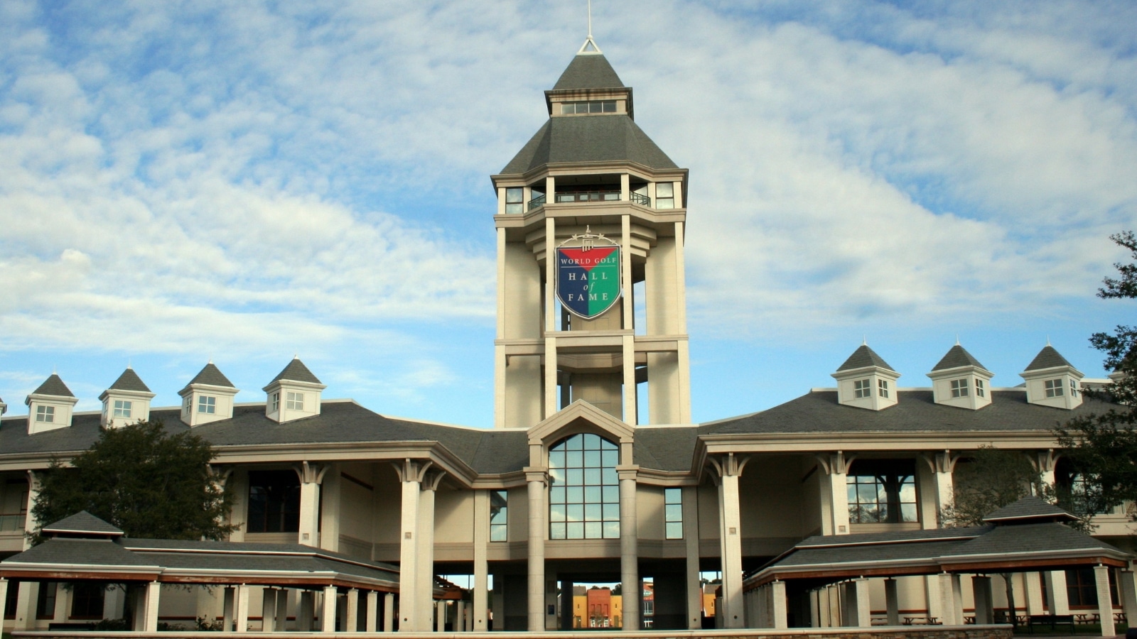 The image features the World Golf Hall of Fame in St. Augustine, Florida. The building's architecture is visible, showcasing a modern design with clean lines and glass panels.