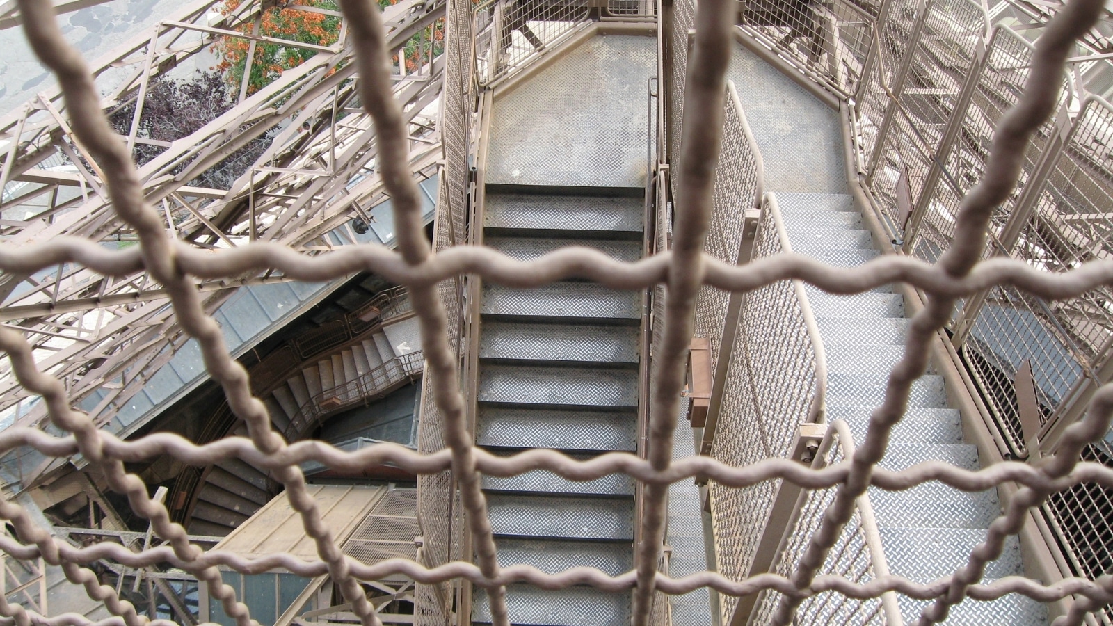 A photograph capturing the stairs leading to the Eiffel Tower in Paris, France. The image features metal protection gates along the staircase, ensuring safety for visitors climbing the iconic monument.