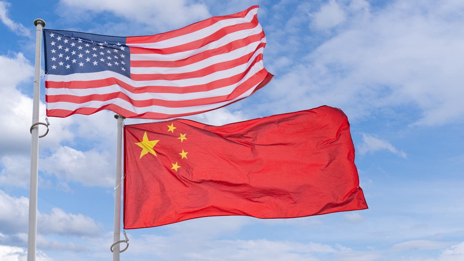 In the image, the American and Chinese flags are depicted fluttering in the wind. The bright colors of the flags stand out against the clear sky in the background.