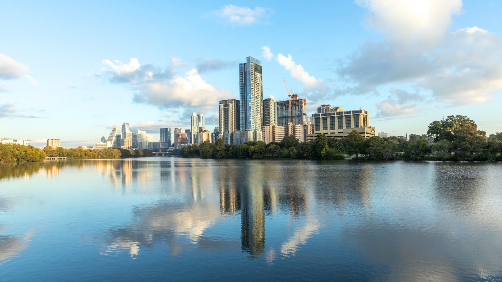 The image captures the skyline of Austin, Texas, illuminated by early morning light, with the city mirrored in the Colorado River. The scene showcases the urban landscape of Austin, with a mix of buildings and structures along the riverbank.