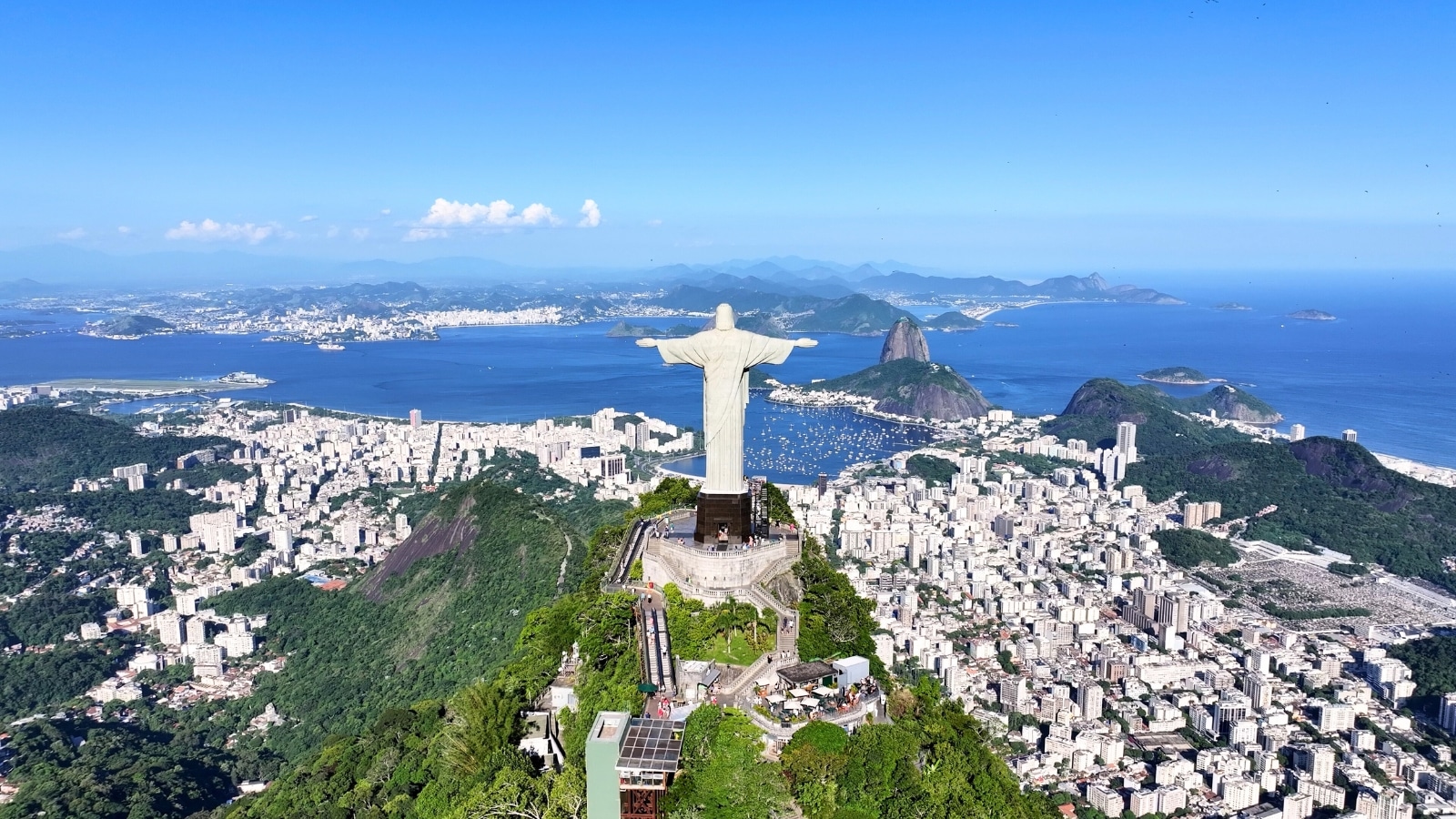 The image captures Christ the Redeemer in Rio de Janeiro, facing the city. It presents a top view of the back of the statue, showcasing the cityscape, mountains, and ocean in the background.