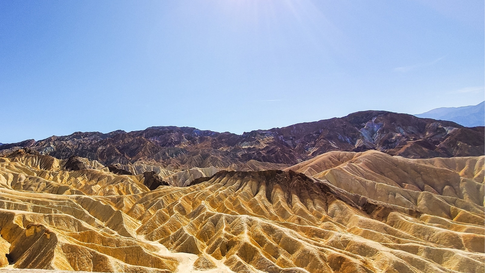 The image depicts Zabriskie Valley in Death Valley National Park, California. The landscape features expansive desert terrain with rugged, eroded hills and valleys. The barren land is characterized by dry, arid conditions and minimal vegetation.