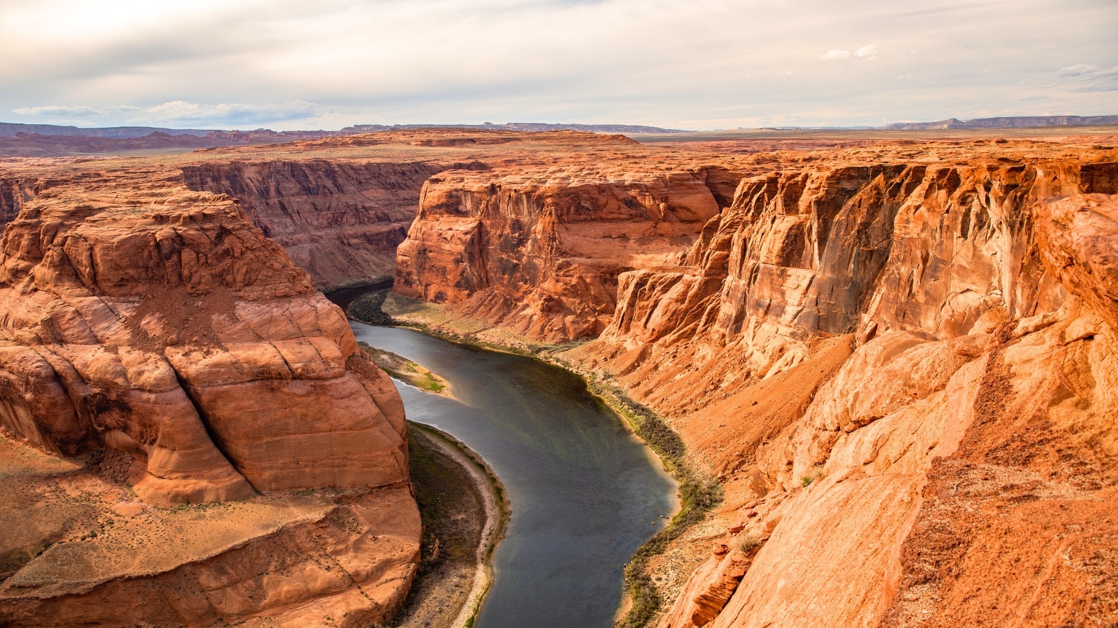 This image captures a panoramic view of the Grand Canyon National Park in Arizona, USA, showcasing the iconic canyon with its rugged terrain and vast expanse. In the center of the frame, a river winds its way through the canyon floor, adding a contrasting element of fluidity against the rocky landscape.