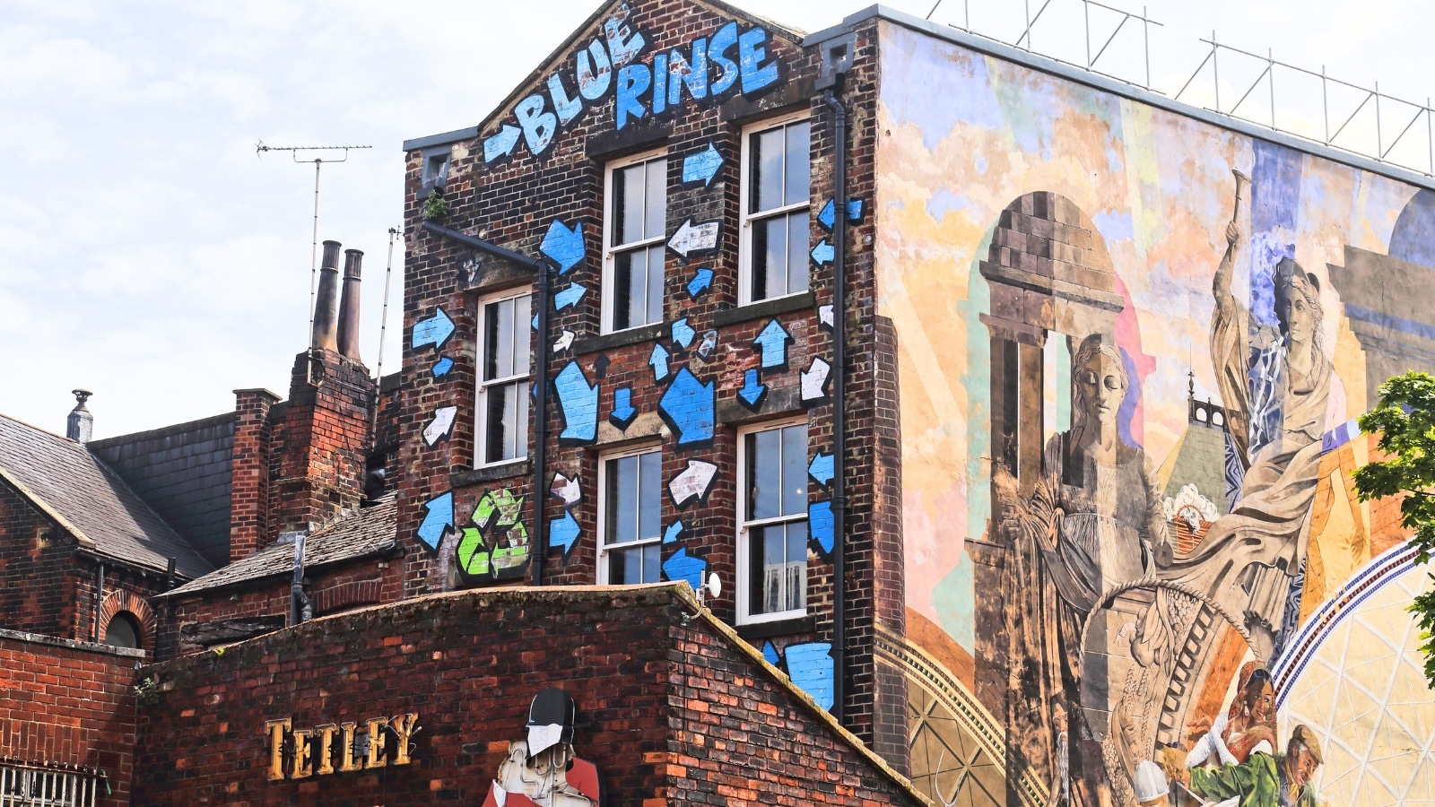 The image captures a scene in Leeds, United Kingdom, showcasing murals and graffiti on old buildings.