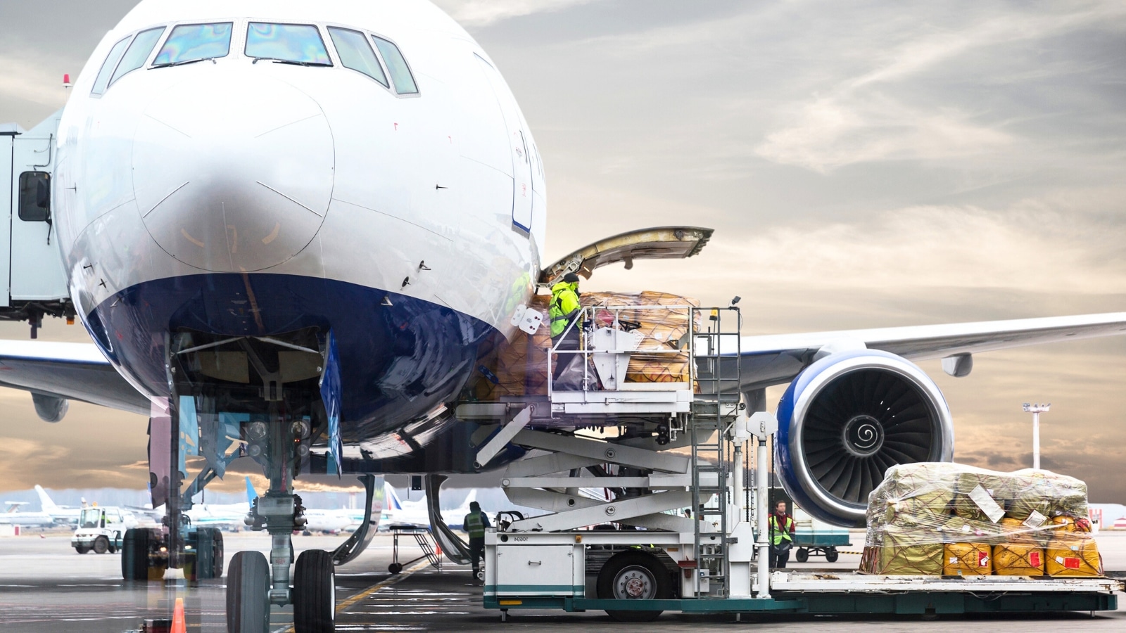 The image depicts the process of loading cargo onto a plane at an airport before a flight.