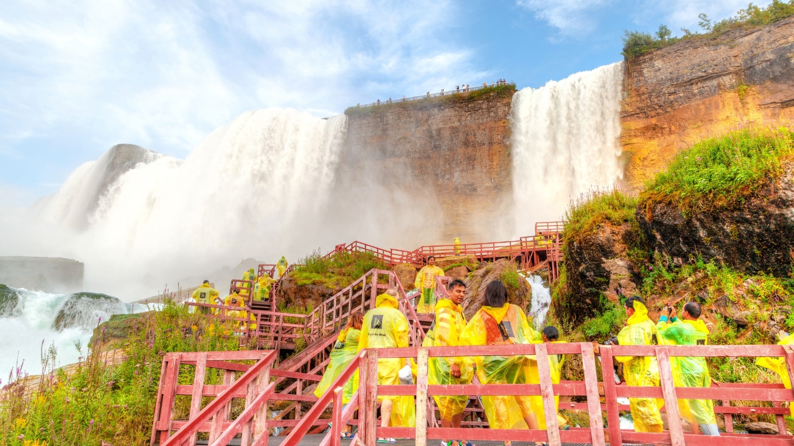 The image captures tourists walking on wooden stairs that lead to Bridal Veil Falls, an offshoot of the American Falls at Niagara Falls, situated between New York, USA, and Ontario, Canada.