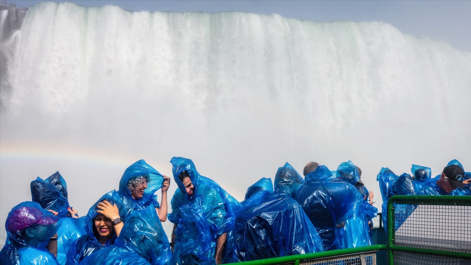 The image captures happy visitors wearing raincoats aboard a tour boat as they experience the splashes of Niagara Falls.