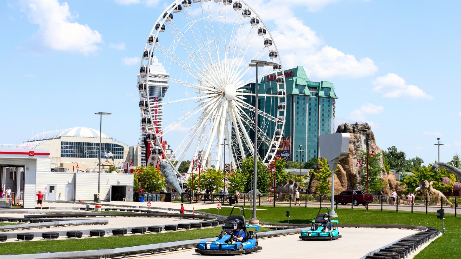 The image captures a view of Niagara Speedway, showing people riding go-karts on the track. In the background, the Niagara SkyWheel is prominently visible.