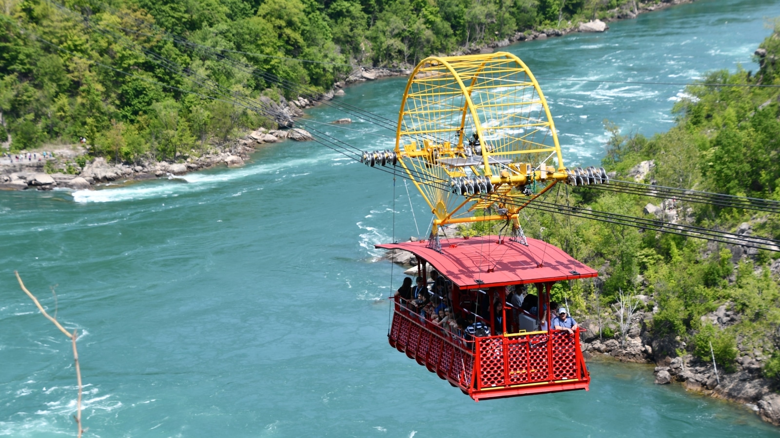 The image captures the Whirlpool Aero Car at Niagara Falls, showcasing a red trolley suspended on ropes with tourists aboard.