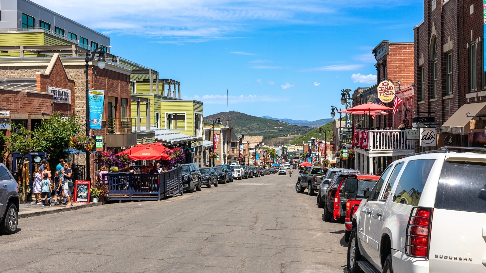 The image showcases Main Street in Park City, Utah, known for its vibrant array of bars, restaurants, and shops. The street is lined with numerous cars parked on both sides.