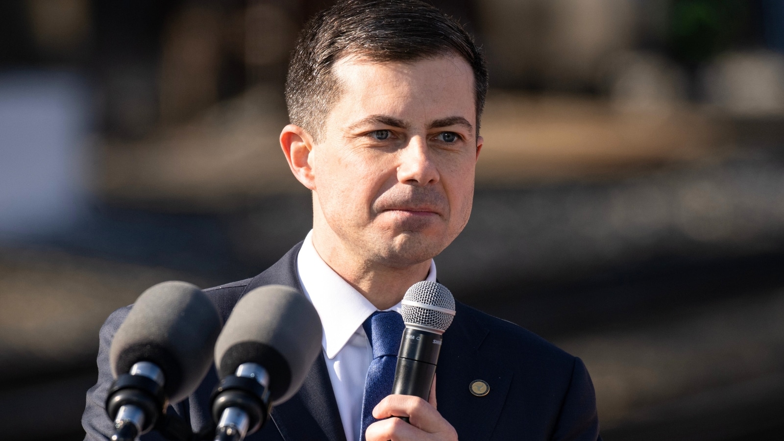 The image features Pete Buttigieg holding a microphone, presumably during a public speaking event.