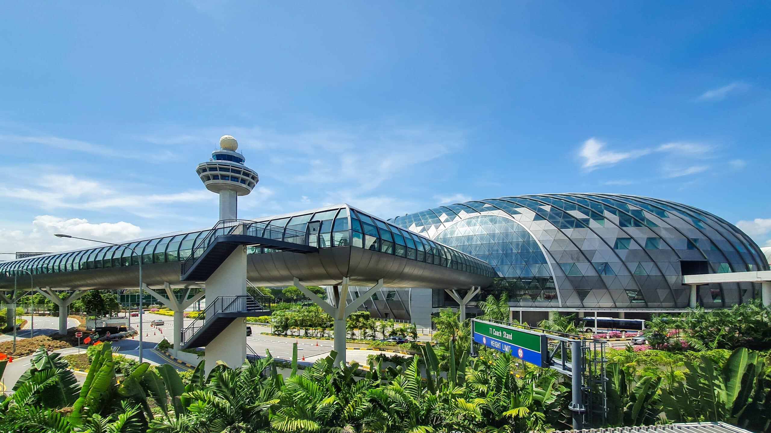 The image showcases an outside view of Jewel Changi and the air traffic control tower of Changi Airport in Changi, Singapore. The airport complex presents a futuristic architectural design, reflecting modernity and innovation. Surrounding the area is an abundance of greenery.