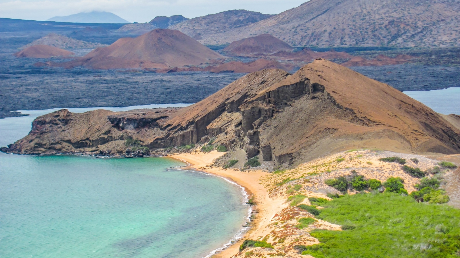 The image features a panoramic view of the Galapagos Islands, captured from the elevated vantage point of Bartolome Island. The scene showcases the natural beauty and geological formations of the islands, including rocky terrain and coastal areas.