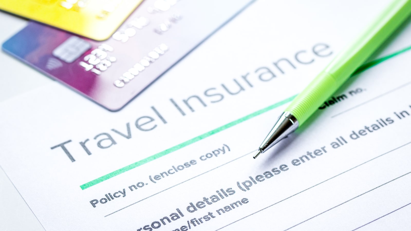 The image shows an insurance form with the title "Travel Insurance" prominently written. Adjacent to the form are two credit cards and a green pen.