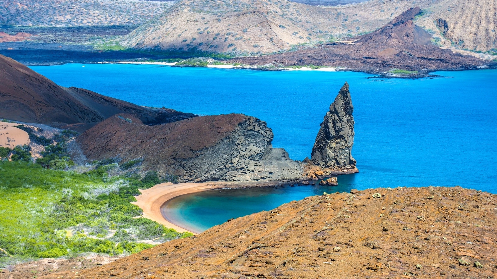 The image captures a view of two beaches on Bartolome Island in the Galapagos Islands, Ecuador. The beaches are distinct, with one featuring white sand and the other showcasing darker volcanic sand. Surrounding the beaches are rocky formations and sparse vegetation typical of the island landscape.