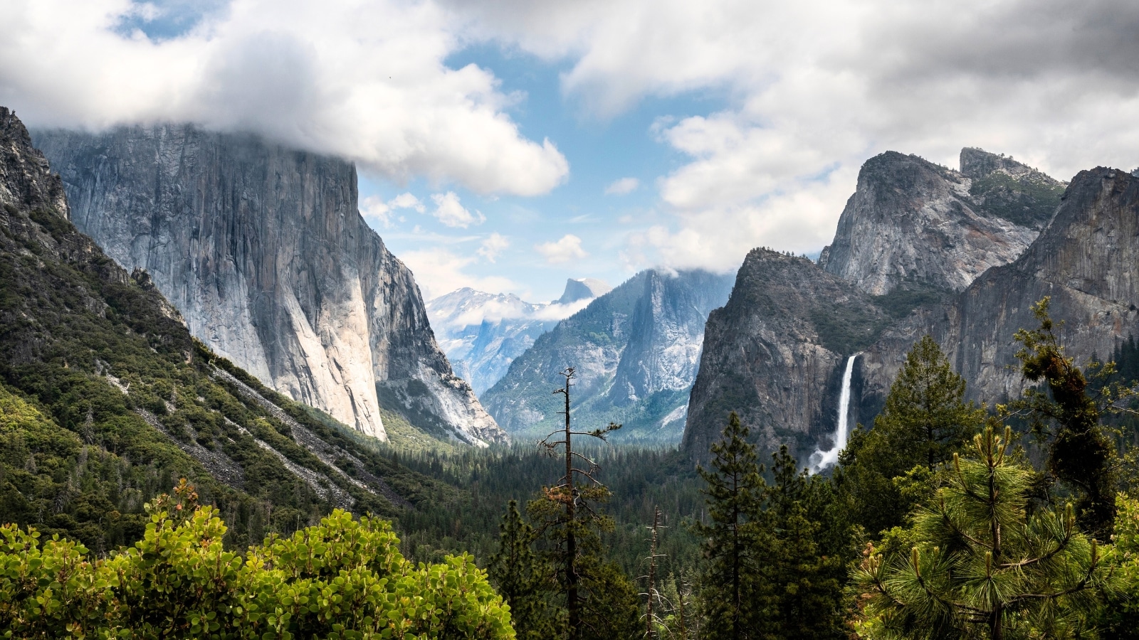 The image captures Yosemite National Park in California, showcasing the iconic Tunnel View with a majestic waterfall in the background.