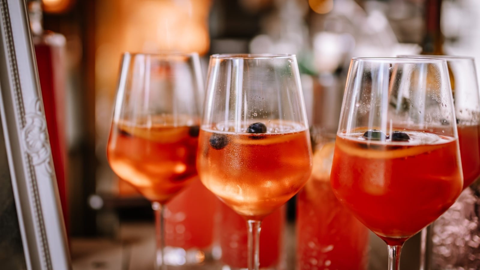 The image showcases a close-up of glasses containing red cocktails, with a blurred background. The cocktails appear vibrant and refreshing, likely made with ingredients that give them their distinct red color.