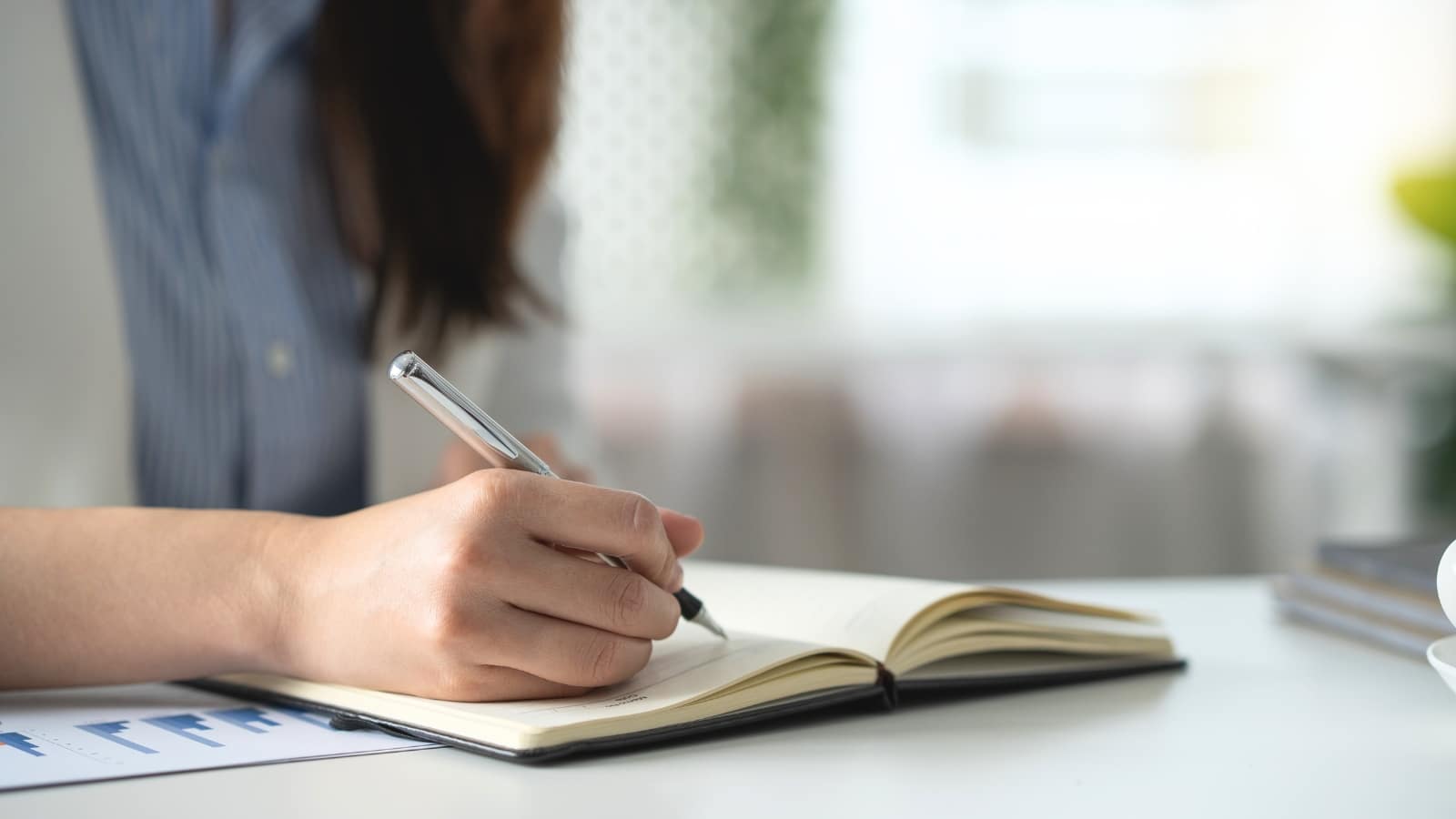 The image depicts a girl sitting with a pen and notepad, engaged in making notes.
