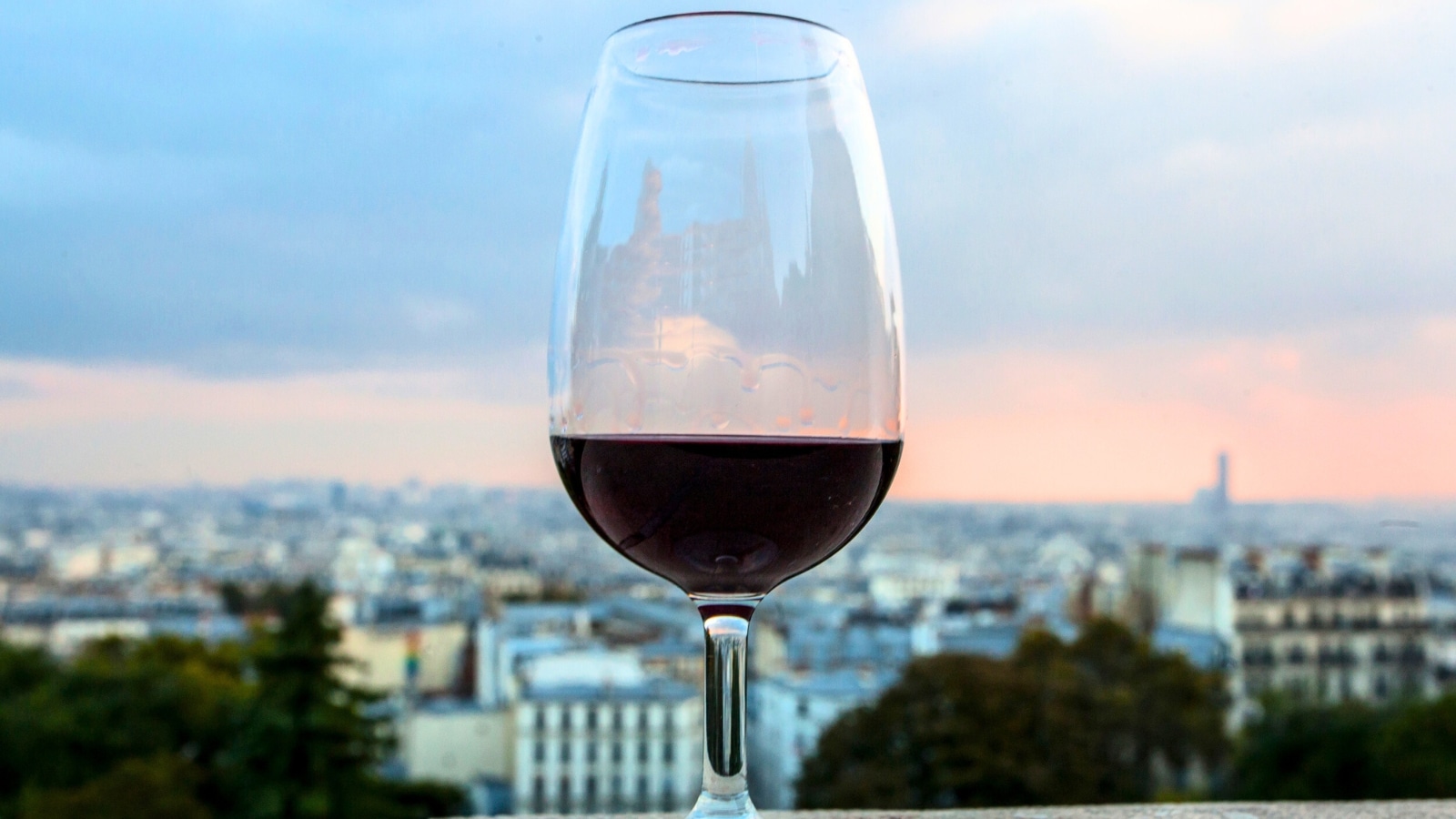 The image captures a top view of a glass of wine in Paris, seen from Montmartre, France. The glass of wine is in focus, with the cityscape in the background intentionally blurred for artistic effect.