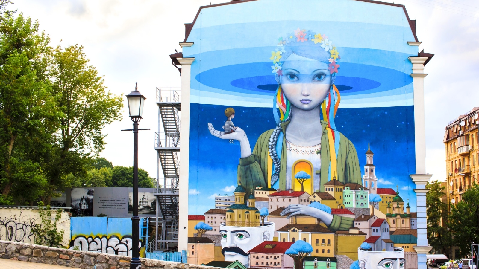 The image showcases a beautiful graffiti painting titled "Revival" located at Andriyivskyy Descent in Kyiv, Ukraine, often referred to as the Montmartre of Kyiv. The painting depicts Ukraine personified as a girl wearing traditional national clothing.