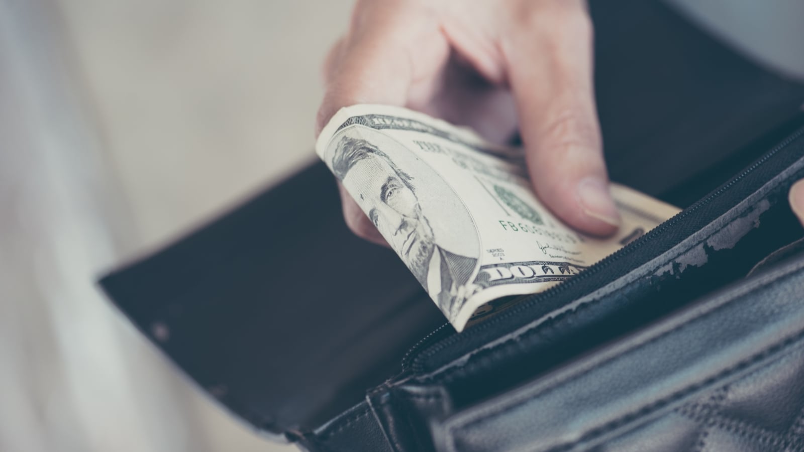 The image depicts a hand withdrawing a bill from a black wallet.