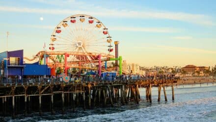 The image presents a close-up view of Santa Monica Pier in Los Angeles, California, featuring a ferris wheel in the background under clear skies.