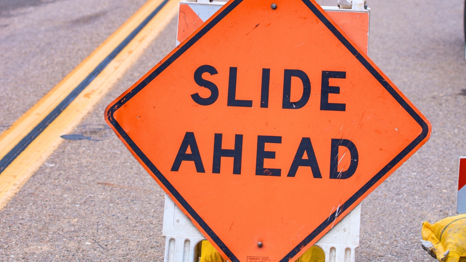 The image displays a road sign with the inscription "Slide Ahead," positioned next to the cones.