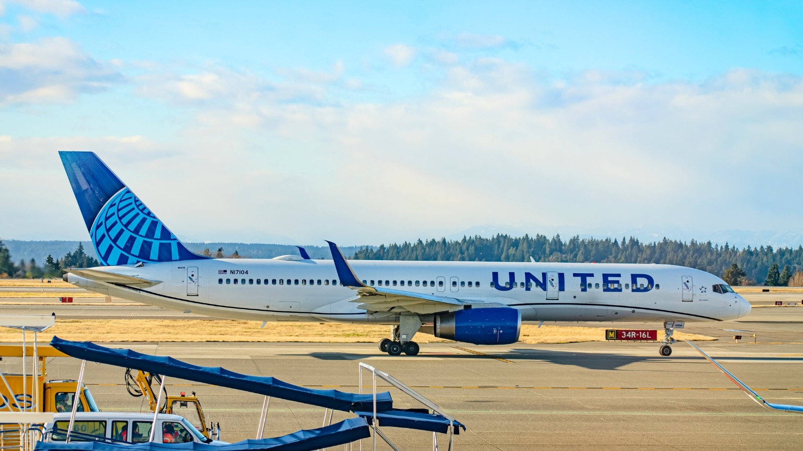 The image shows a United Airlines Boeing 757 aircraft taxiing toward the runway in preparation for take-off. The airplane prominently displays the United lettering and features a blue tail.