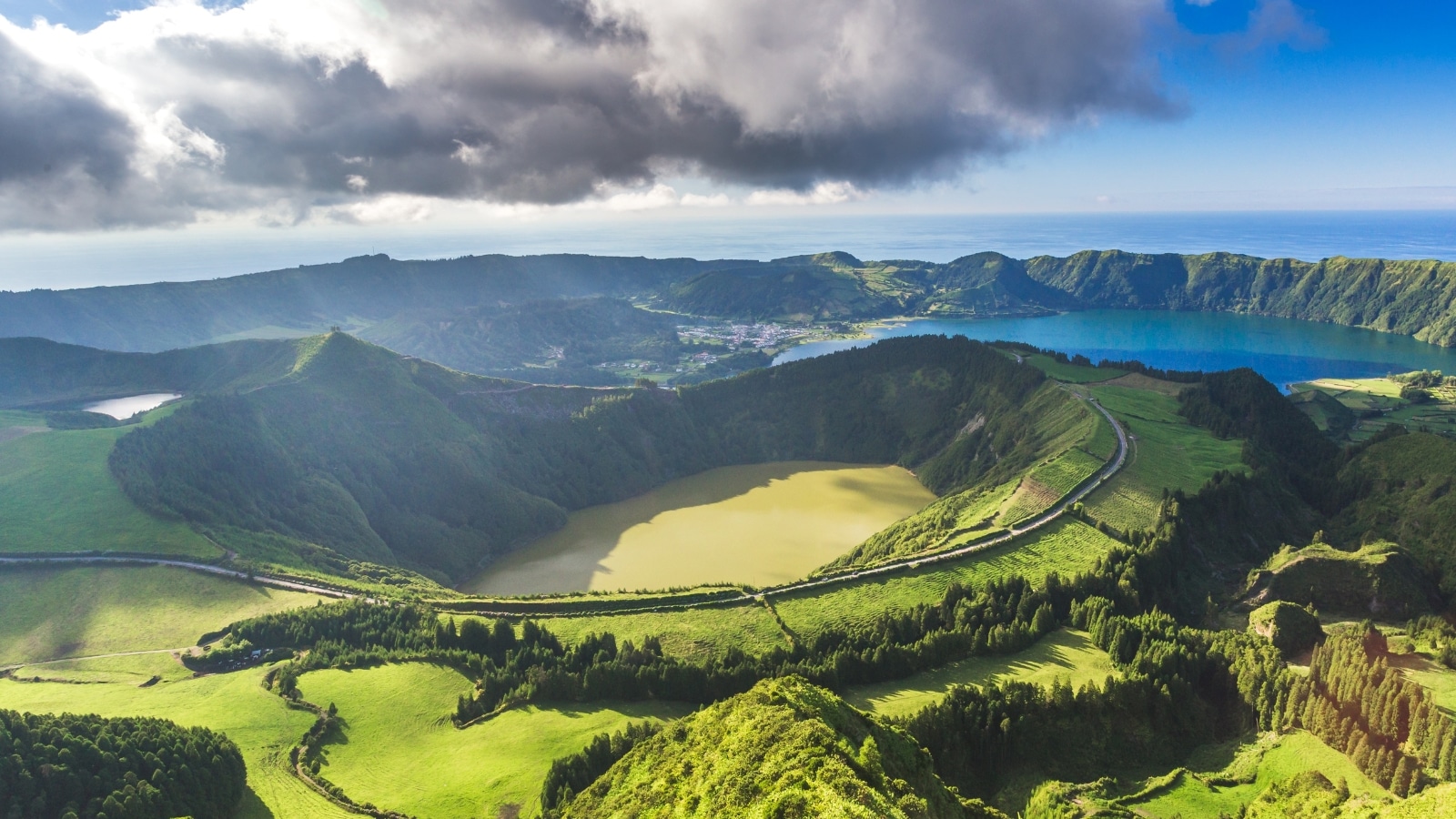 Sete Cidades near the Miradouro da Grota do Inferno viewpoint on Sao Miguel Island, Azores, Portugal. The landscape features lush greenery and rolling hills, characteristic of the Azores archipelago. In the distance, the twin lakes of Sete Cidades, one blue and the other green.