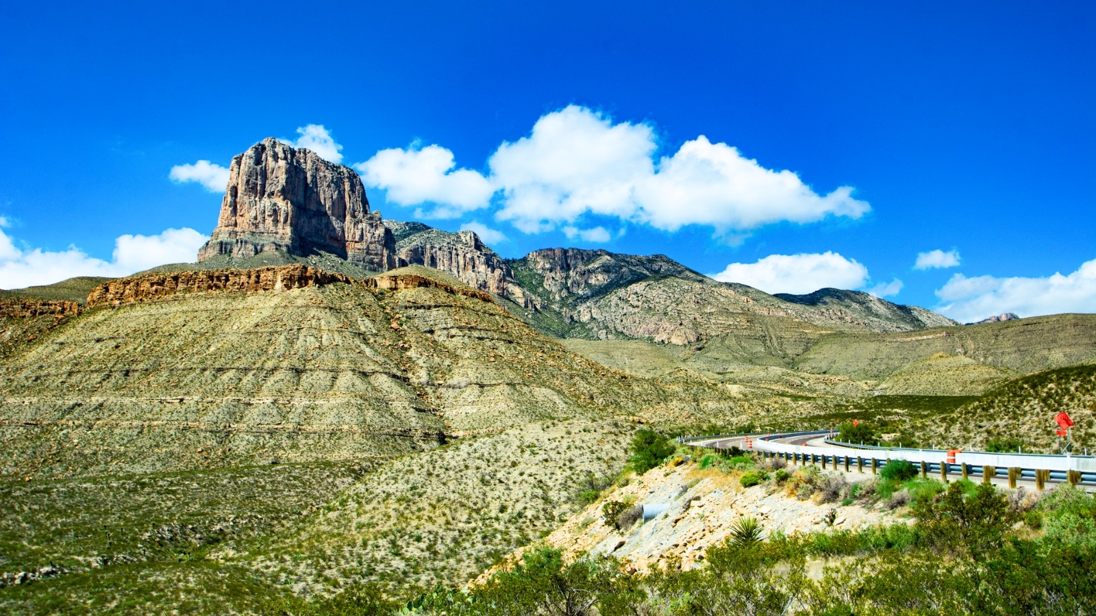 In Guadalupe Mountains National Park, Texas, USA, the image features a rocky mountain set against a clear blue sky with small clouds.