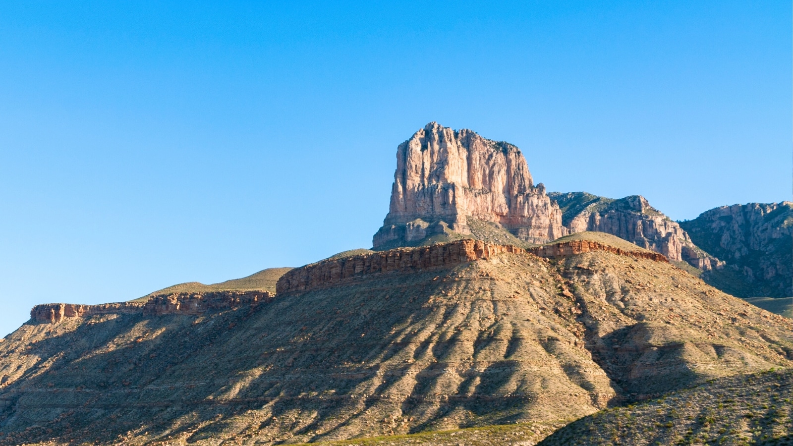 El Capitan at Guadalupe Mountains National Park in Western Texas, USA. The mountain features a high rock formation, characteristic of the rugged terrain in the region. The sky is clear, devoid of clouds, emphasizing the vastness of the landscape.