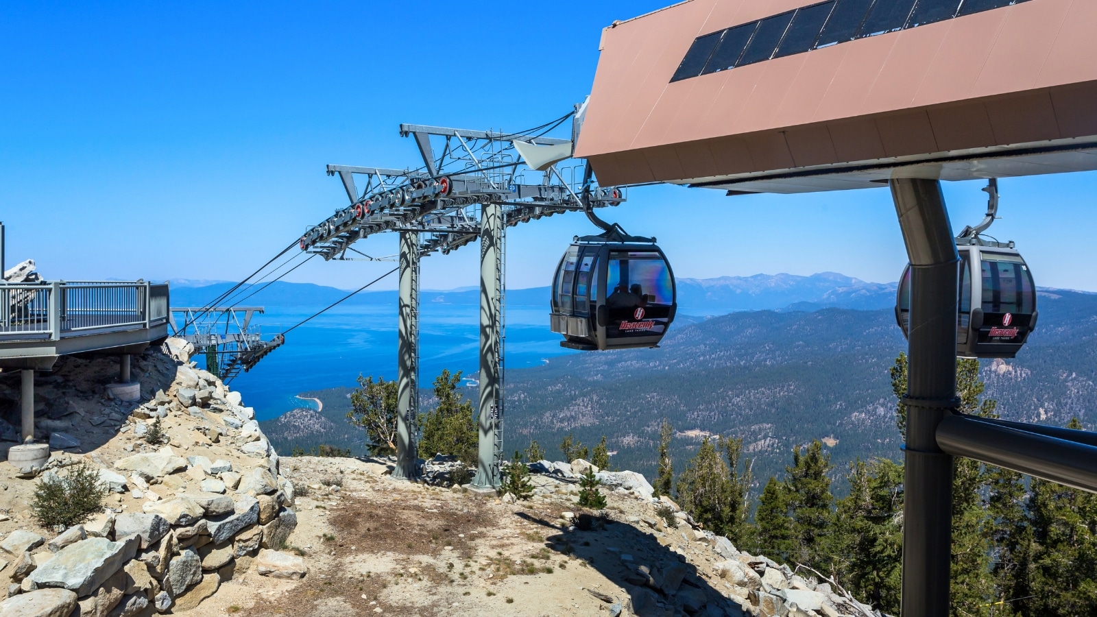 South Lake Tahoe, California, featuring the Heavenly Gondola Ride during summer. The focus is on the iron structure of the lift, with two closed carts suspended on cables. The sky appears clear.