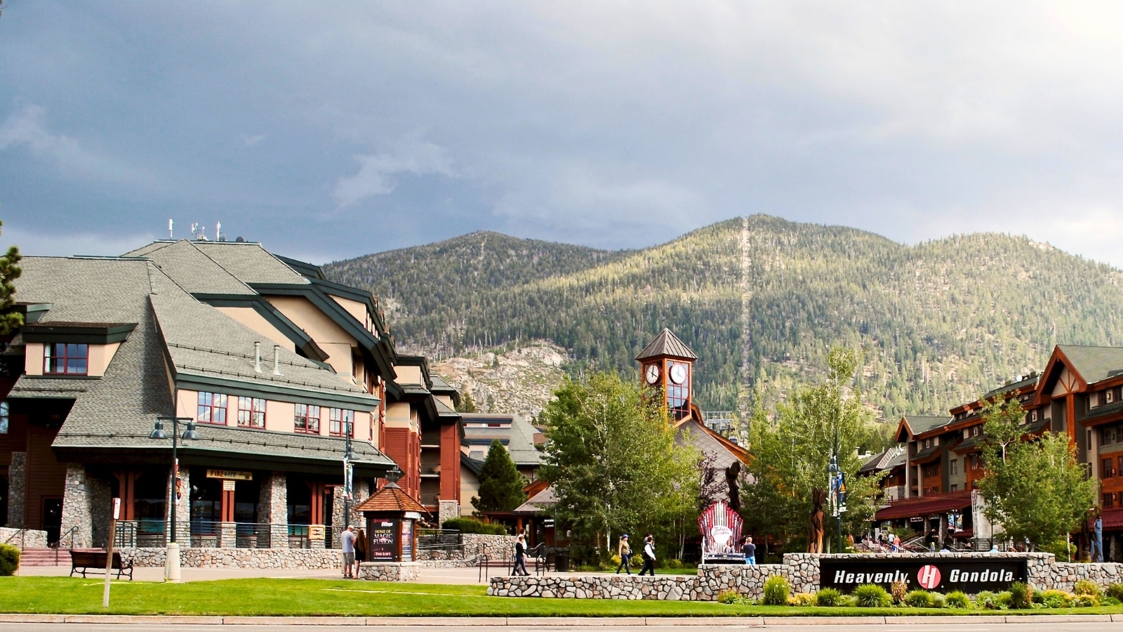 Sky Village in South Lake Tahoe, California, under an overcast sky. In the foreground, there is a hotel complex with dark roofs, blending into the natural surroundings.