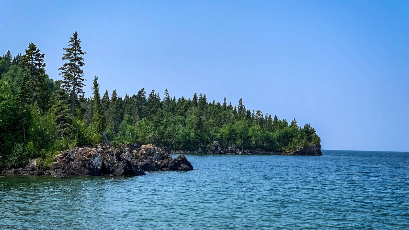 Isle Royale National Park in Michigan, featuring an ocean in the foreground and a park forest with a rocky shore in the background. The composition captures the natural beauty and diverse landscapes of the park, highlighting its coastal and wooded areas.
