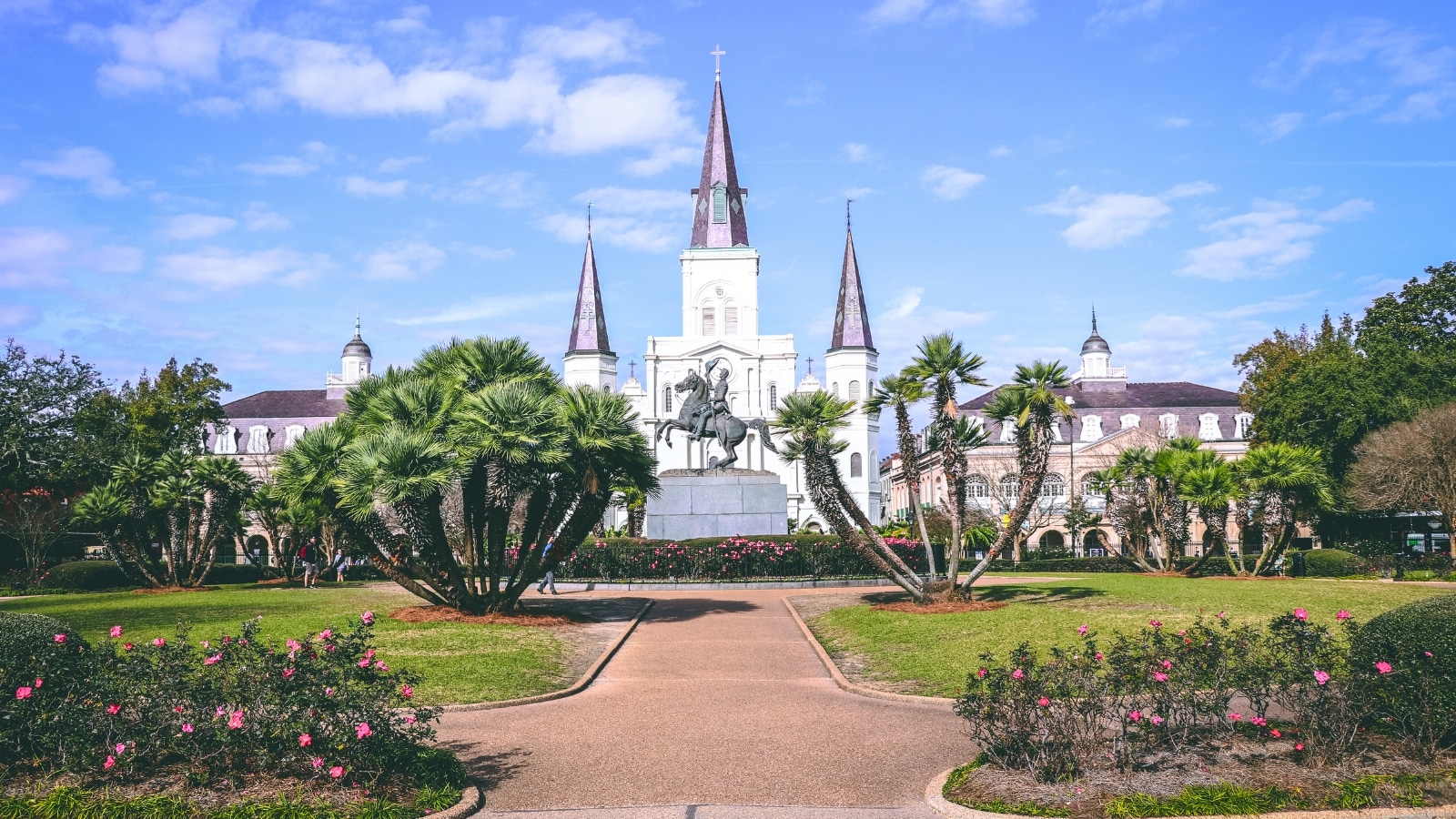 St. Louis Cathedral in New Orleans features a striking facade with three spires and intricate architectural details. The structure is primarily white with dark accents, creating a sharp contrast. The cathedral consists of large doors, arched windows, and a central clock.