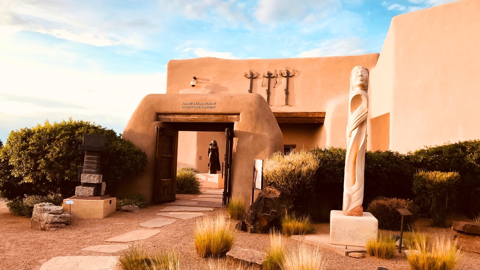 The entrance to the Sculpture Garden at the New Mexico Museum of Indian Arts and Culture in Santa Fe, New Mexico, presents a welcoming and artistic ambiance. The pathway leading to the garden is lined with native plants and sculptures, hinting at the cultural richness within.