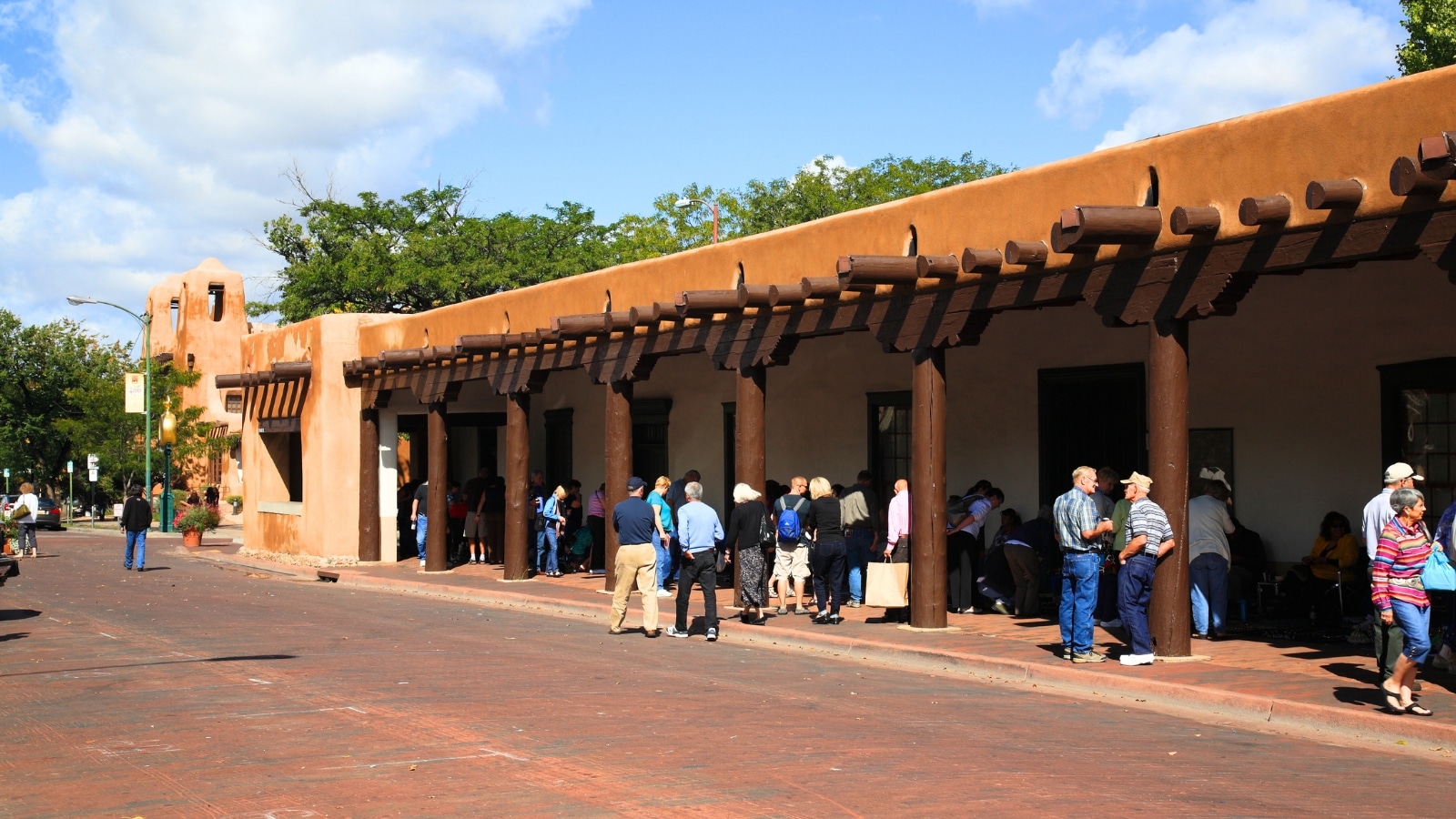 In Santa Fe, New Mexico, the scene captures shoppers and tourists bustling at a Native American market. The market is roofed, providing shade for traders and visitors alike.
