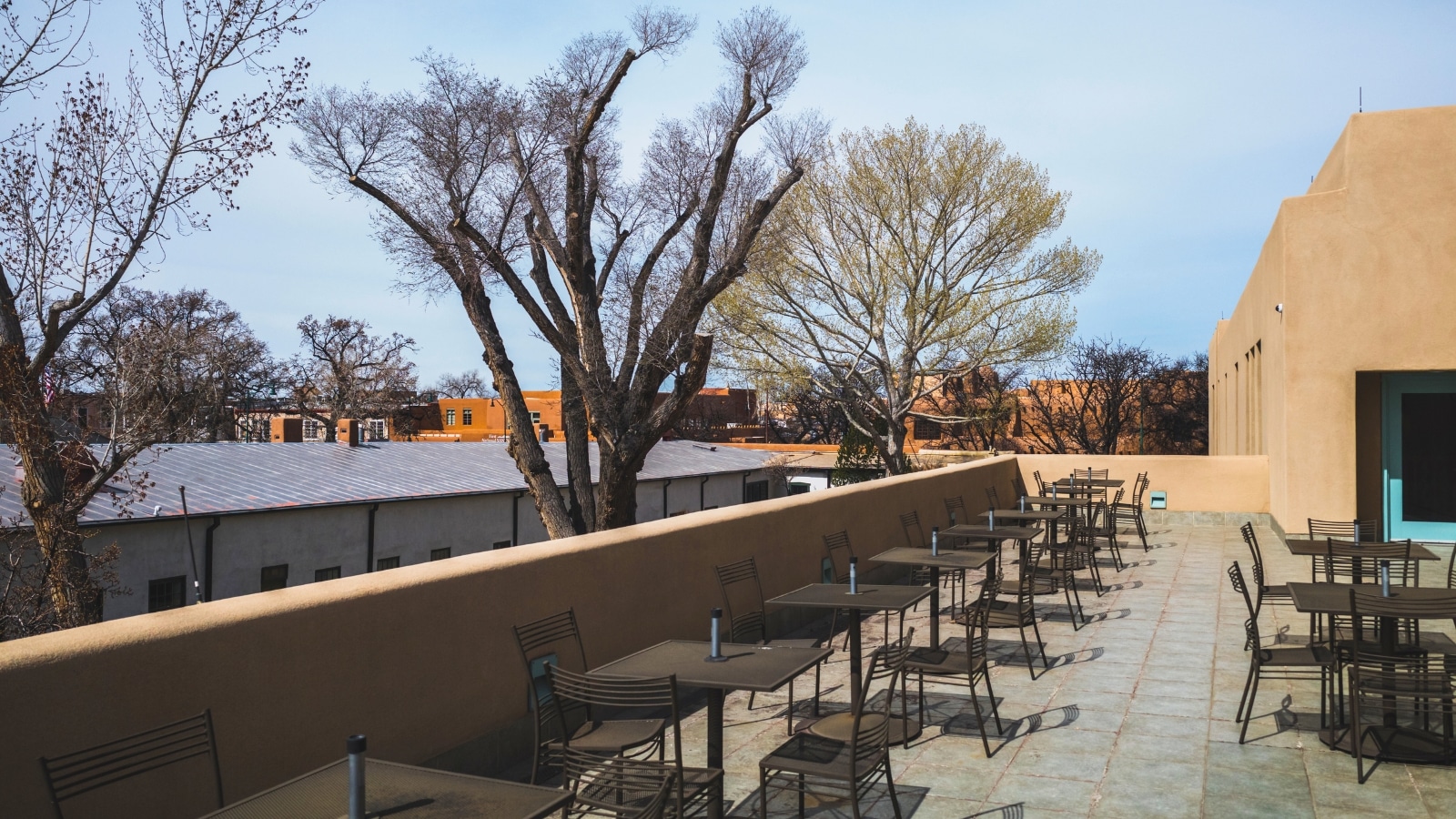 In Santa Fe, New Mexico, the image shows outdoor seating on the terrace of the New Mexico History Museum, providing a picturesque view of downtown. The terrace consists of tables and chairs arranged neatly.
